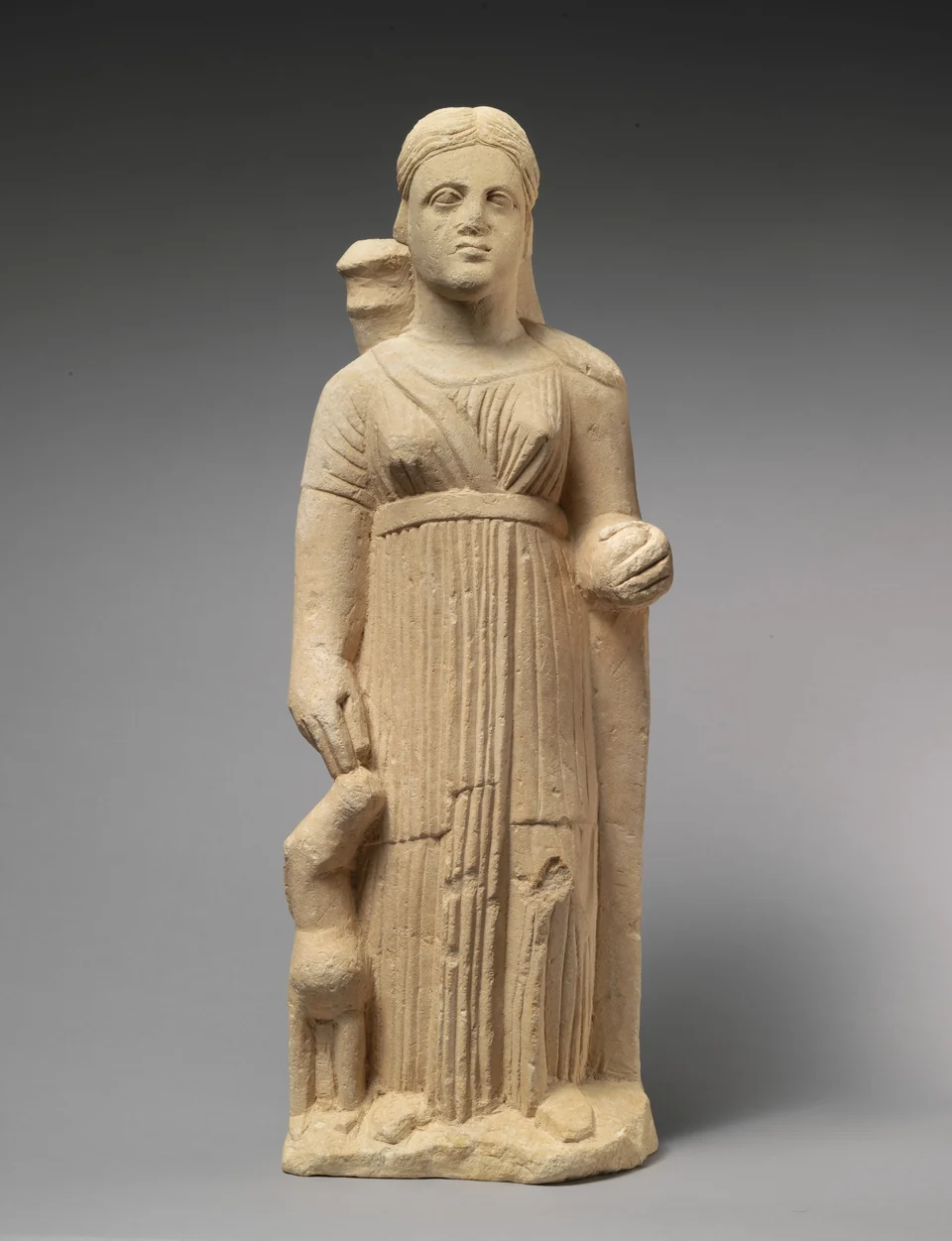 Zyprische Kalksteinfigur einer stehenden Frau mit Köcher und jungem Reh vor dunklem Studiohintergrund.