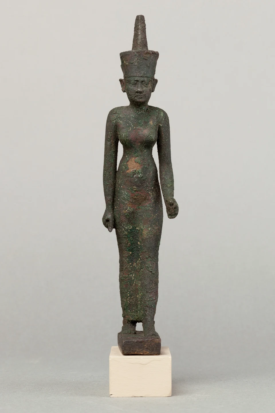 Stehende dunkel patinierte Bronzefigur Neiths mit hoher roter Krone; die gehaltenen Gegenstände fehlen.