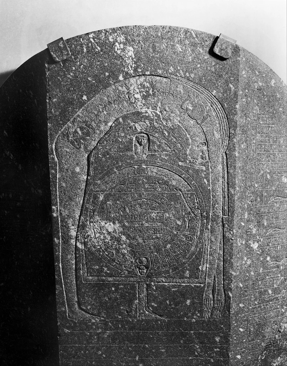 Schwarzweissfoto der gerundeten Sarkophag-Kopfseite: Eine grosse gebogene Gestalt umrahmt mehrere konzentrische Bildringe; Relief und Inschrift sind stellenweise abgerieben.