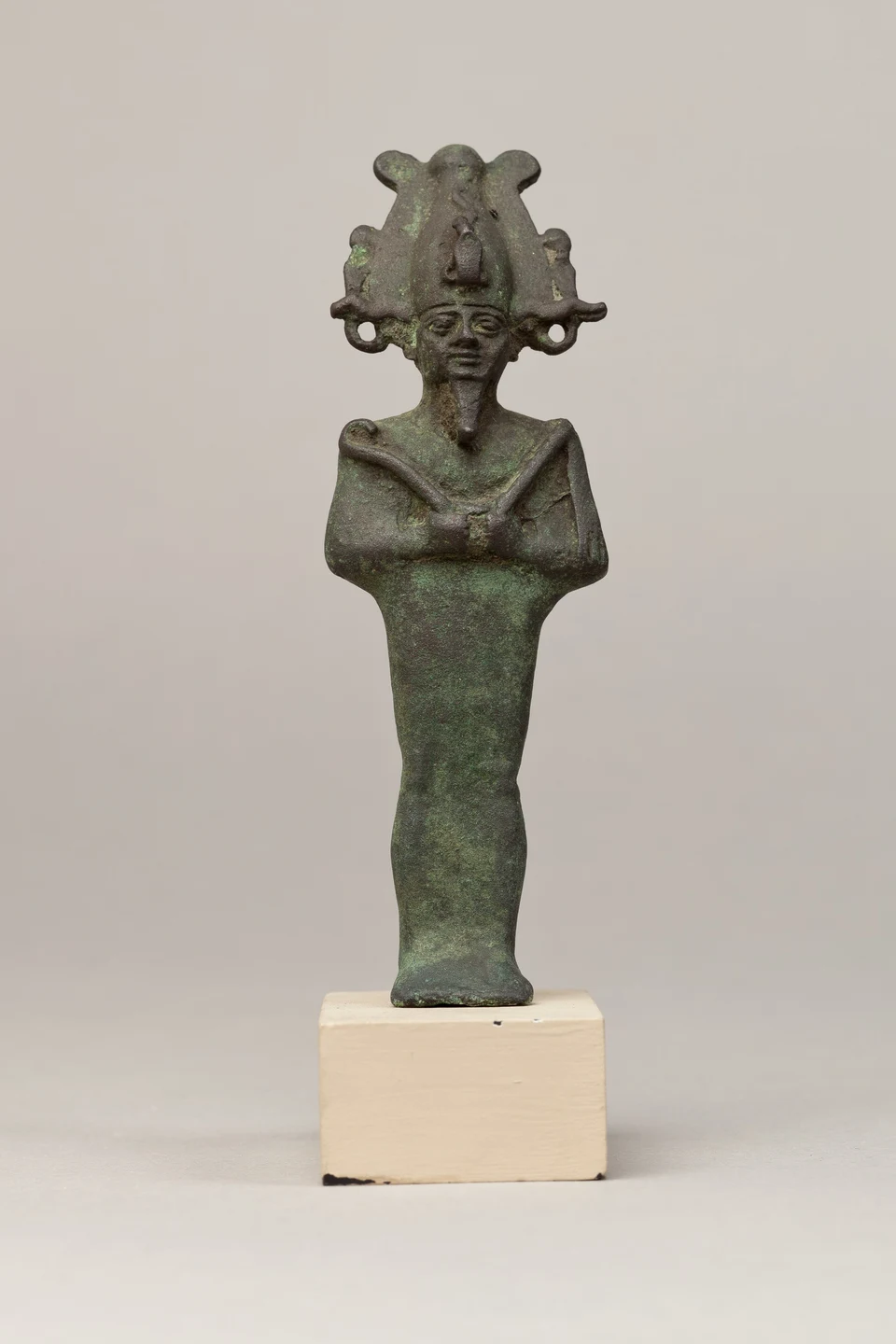 Dunkle Metallstatuette des stehenden Osiris mit hoher Krone und vor der Brust gekreuzten Armen.