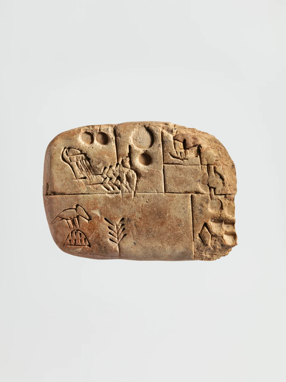 Kleine querrechteckige Tontafel mit abgerundeten Ecken, eingeritzten Feldern, kreisförmigen Vertiefungen und unterschiedlichen Zeichen; an der rechten Kante ist die Oberfläche beschädigt.
