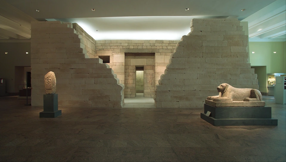 Frontale Museumsansicht von Pernebs Grabbau: Steinwände öffnen in der Mitte den Blick auf Hof und inneren Eingang. Decke, Licht und andere ausgestellte Objekte zeigen den heutigen Museumskontext.