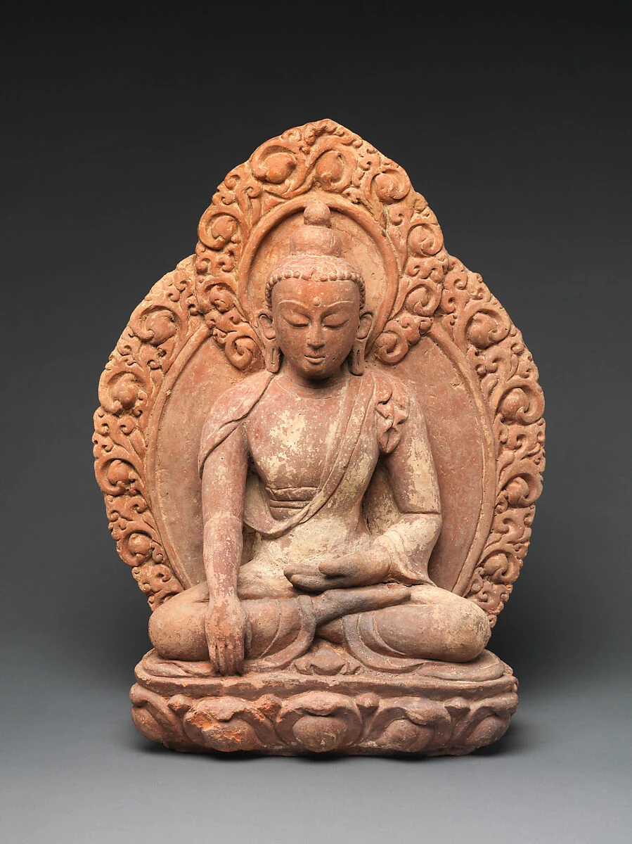 Rostrote sitzende Tonfigur vor einem ovalen, ornamentierten Nimbus; eine Hand liegt im Schoß, die andere reicht am Knie nach unten.