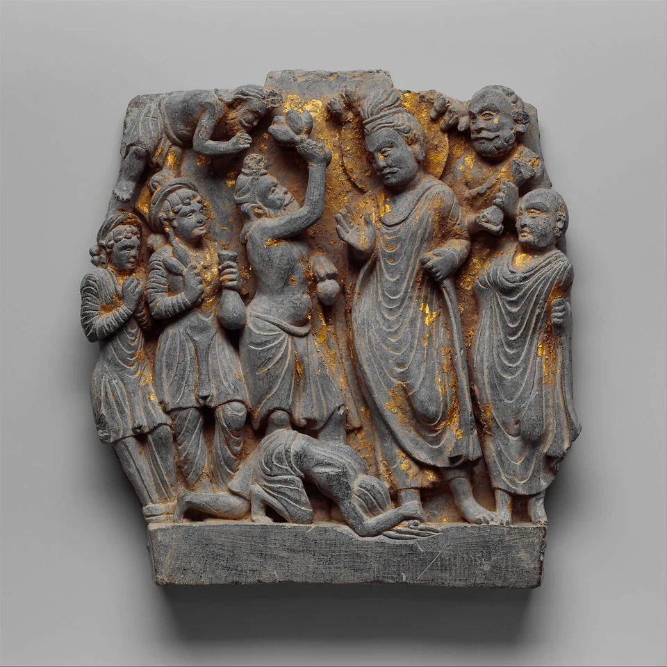 Dunkles Steinrelief mit Goldspuren: eine große stehende Figur, eine am Boden liegende Gestalt und weitere Figuren, darunter eine mit erhobenen Blumen.