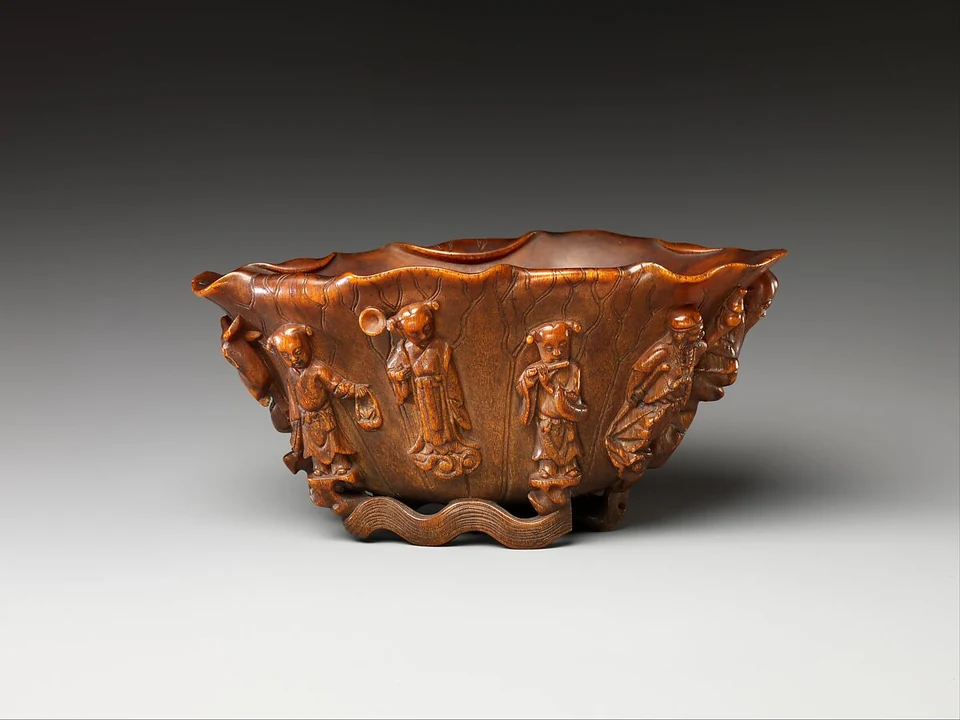 Brauner geschnitzter Becher mit mehreren Figuren und unterschiedlich gehaltenen Gegenständen, Ansicht A.
