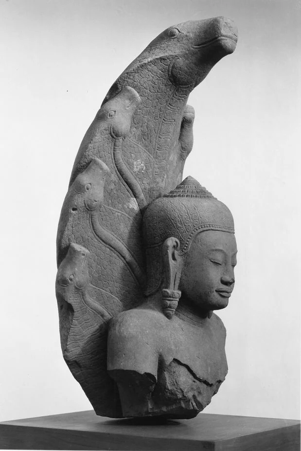 Dreiviertelansicht eines gebrochenen Buddha-Oberkörpers und einer Haube mit mehreren Schlangenköpfen vor hellem Hintergrund.