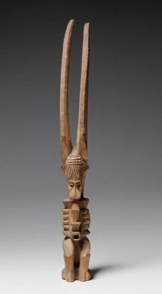 Eine kleine geschnitzte Holzfigur mit zwei langen aufragenden Hörnern, gestuftem Oberkörper und kurzen Beinen.