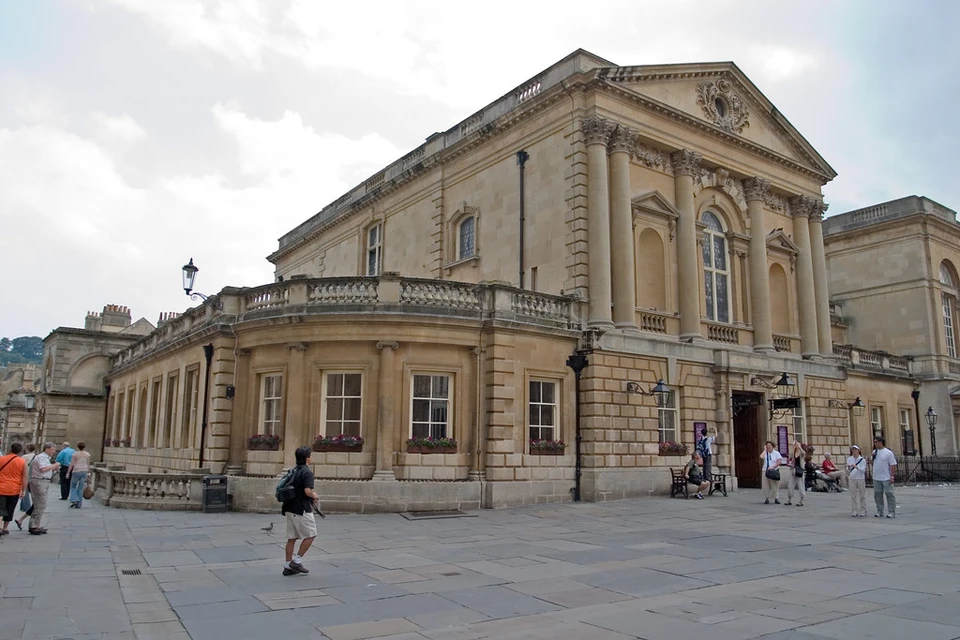 Außenansicht des Bath-Museumszugangs mit Säulen, Giebel und Besuchenden auf dem Platz; keine antike Tempelfassade.