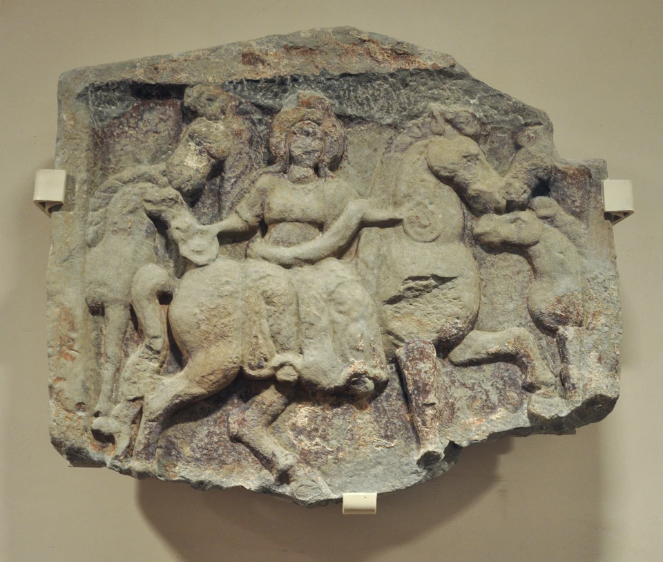 Steinrelief im Vorarlberg Museum: Eine sitzende Frauengestalt ist von mehreren Pferden umgeben; Bruch- und Verwitterungsspuren bleiben sichtbar.