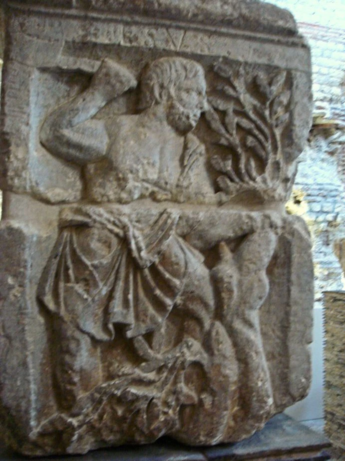 Esus-Relief am Pariser Nautenpfeiler: menschliche Gestalt mit erhobenem Werkzeug neben einem Baum; Bruchstellen und begrenzte Bildschärfe sind sichtbar.