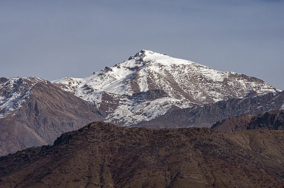 Der Berg Mereto mit Schneeflecken, dunklen kahlen Vorderhängen und blaugrauem Himmel.