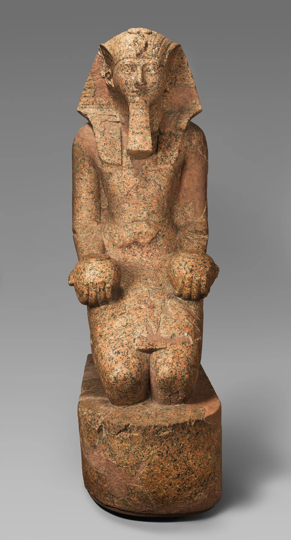 Frontal fotografierte große kniende Statue der Hatschepsut aus rötlichem Stein mit Königskopftuch und falschem Bart.