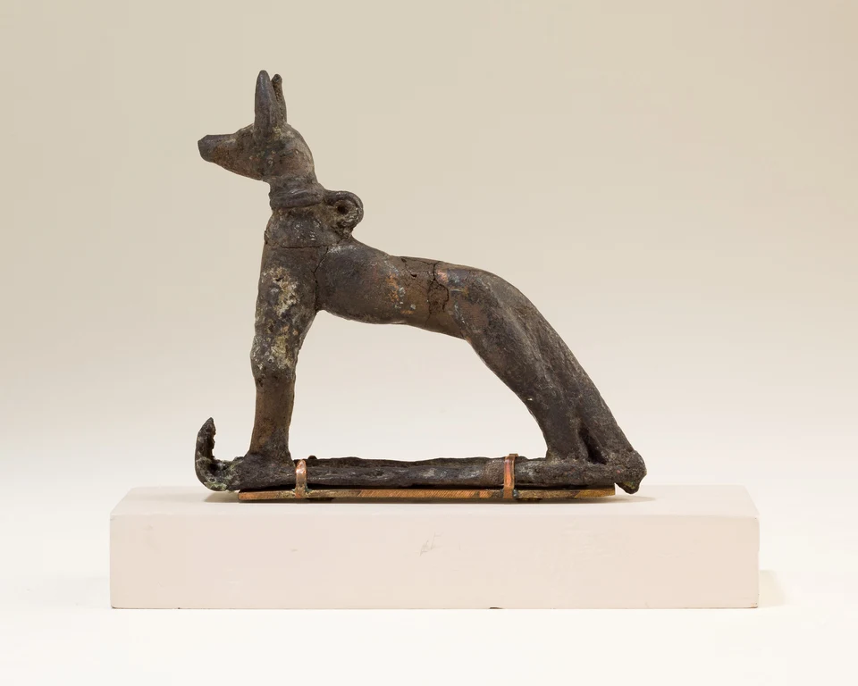 Dunkle kleine Tierfigur Wepwawets mit aufgestellten Ohren auf einem länglichen Schlitten, am Hals eine Öse.