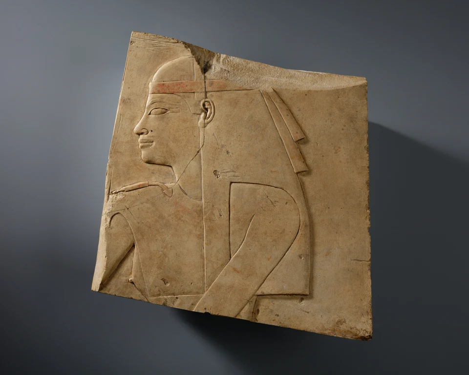 Fragmentiertes helles Kalksteinrelief mit Profilkopf und Oberkörper einer Göttin; Kopfschmuck oben abgebrochen.